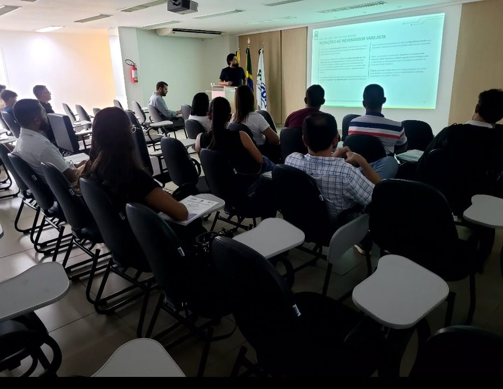 Vista geral do curso Conhecendo o Mercado de Combustíveis, com palestrante, bandeiras e plateia